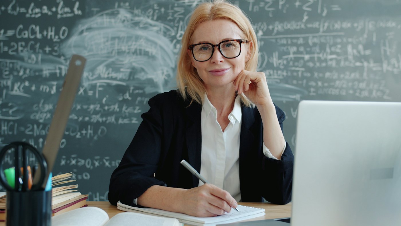 Lehrerin lächelt am Pult mit Laptop